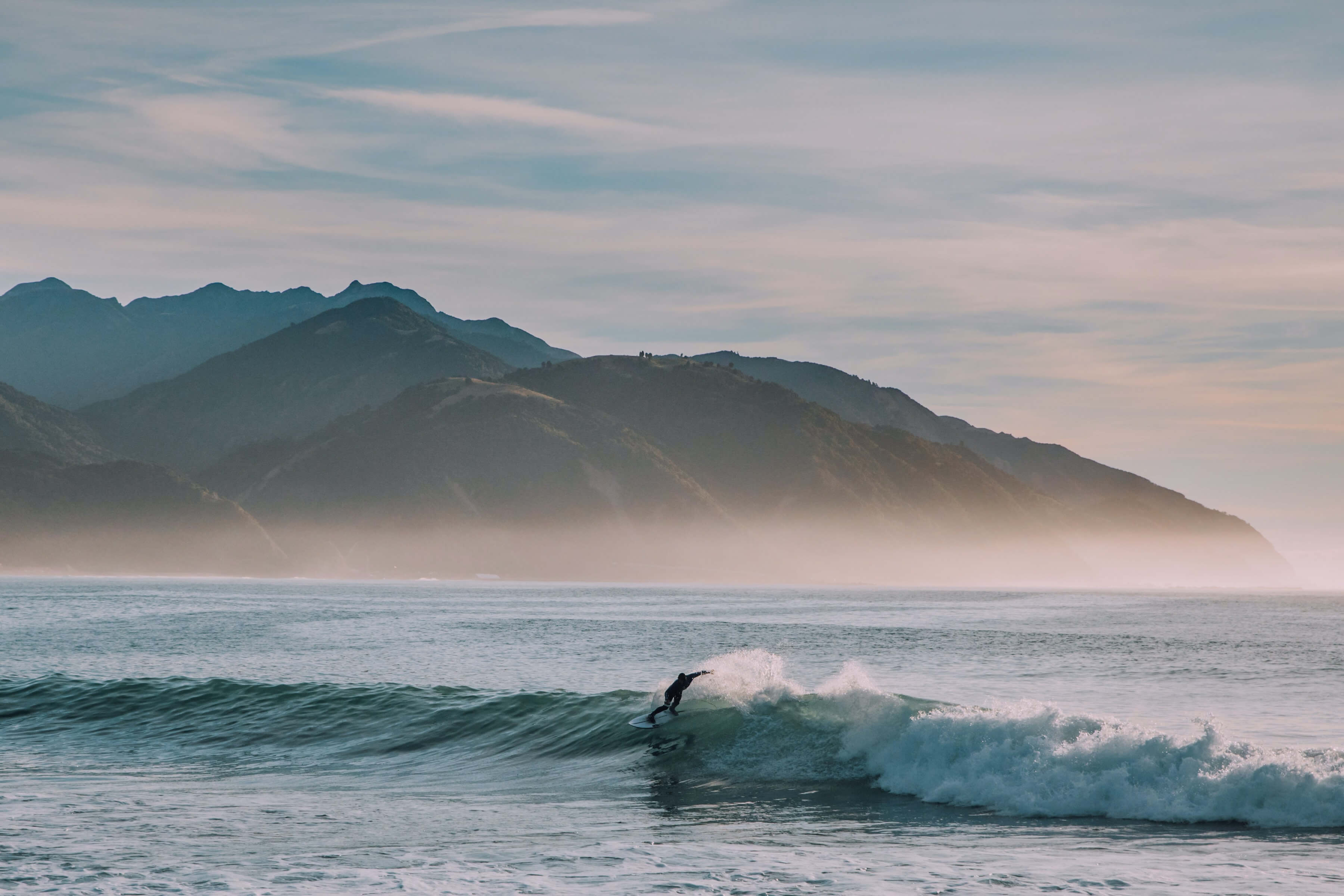 Surfer riding a wave in front of Kaikoura mountains