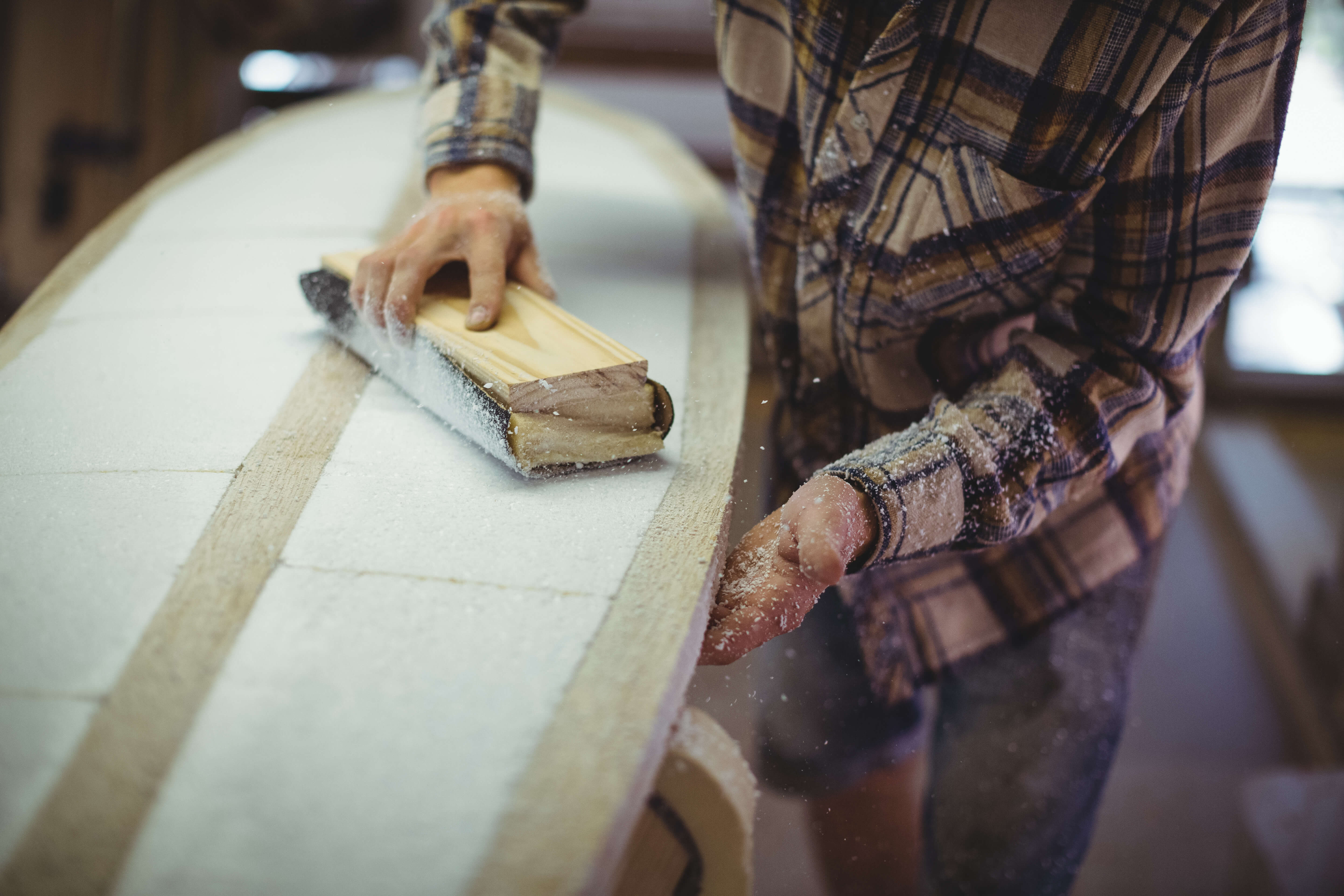 Close up photo of a mans torso whilst he sands down a surfboard in a workshop