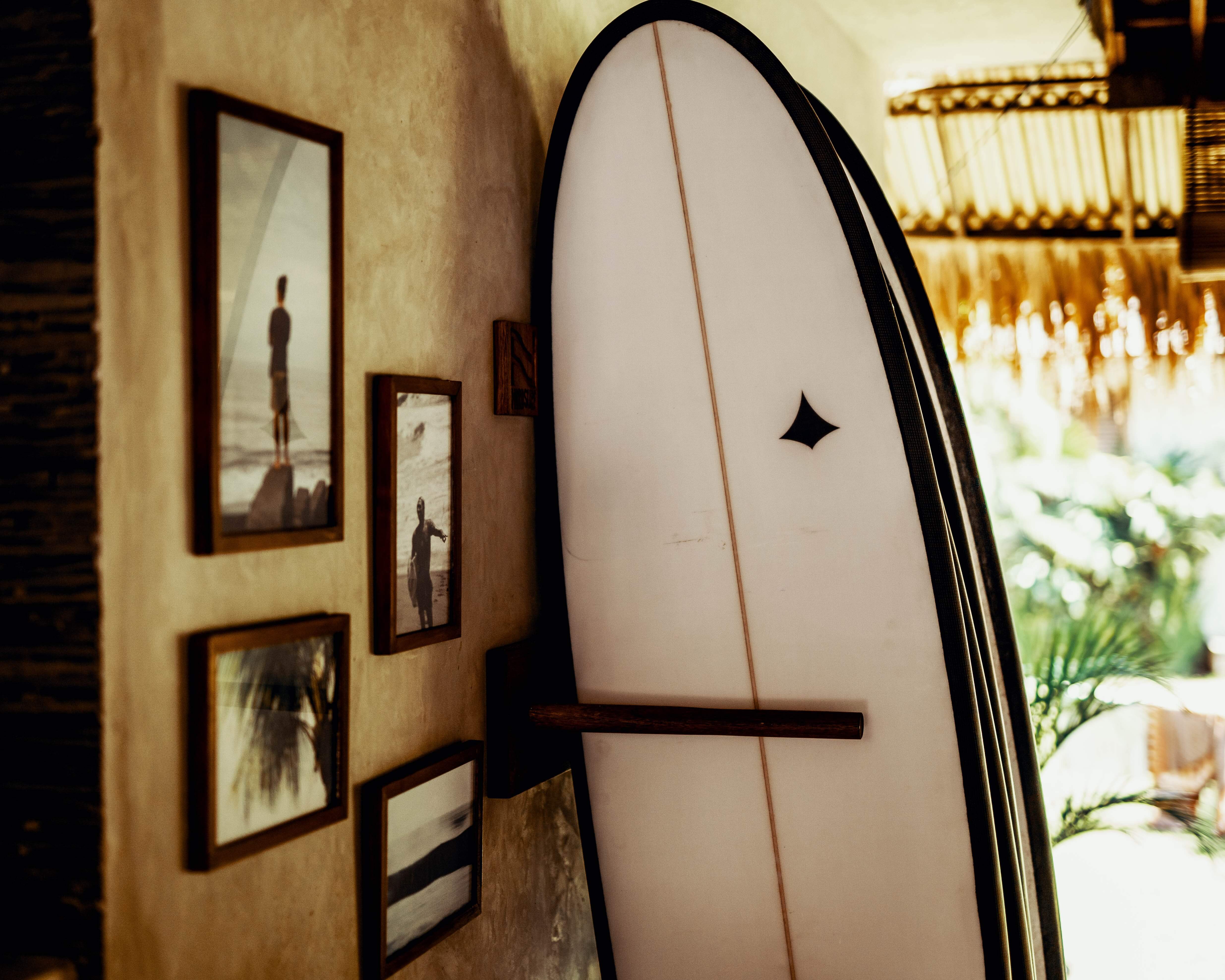 Row of surfboards in a rack against a wall with picture frames hanging and the sun in the background