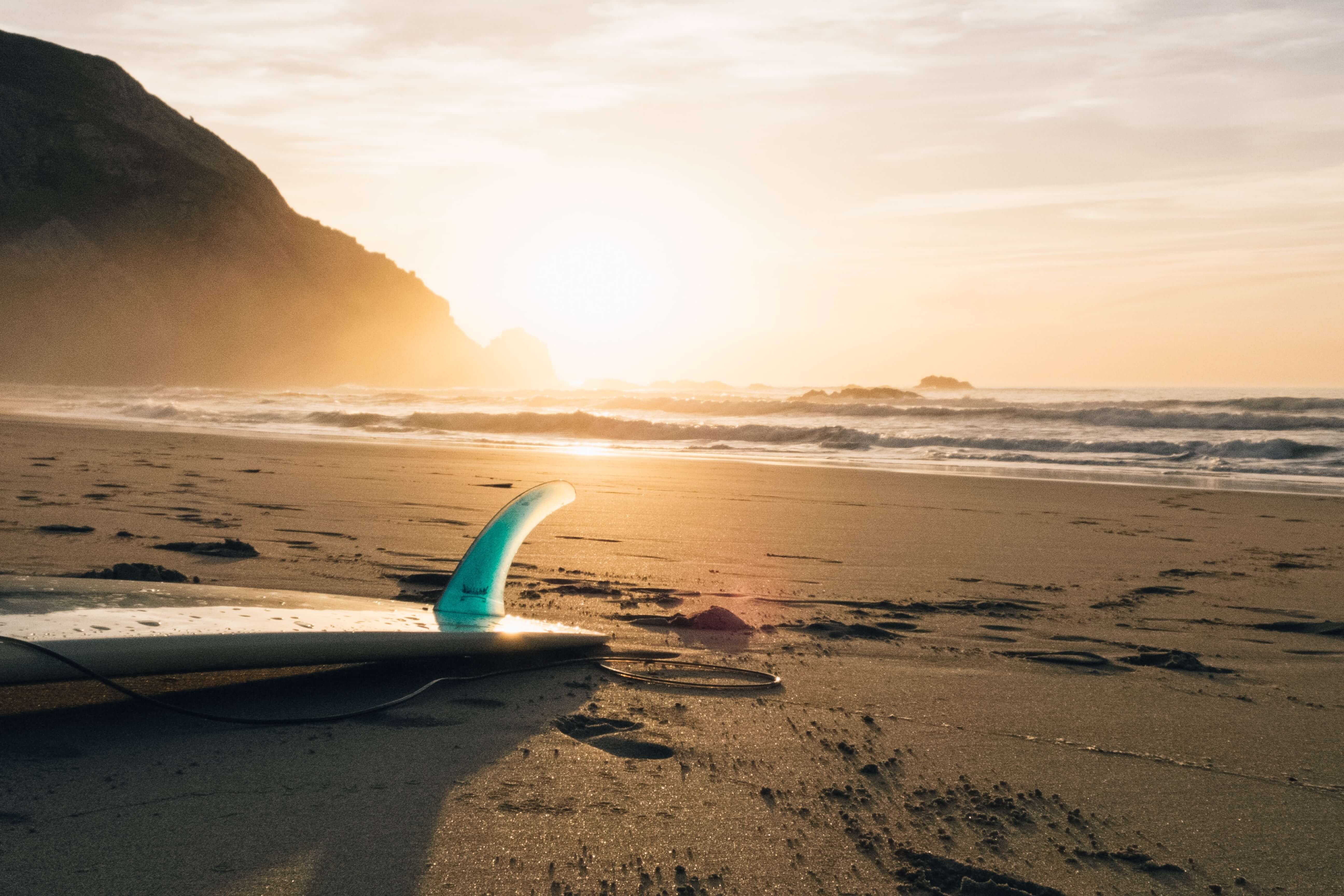 Surfboard laying down with the fin pointing up with the sunset
                    in the background over the ocean
